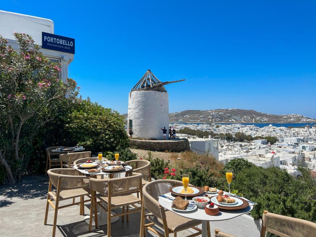 einen Tisch und Stühle mit einer Windmühle im Hintergrund in der Unterkunft Portobello Boutique Hotel in Mykonos Stadt