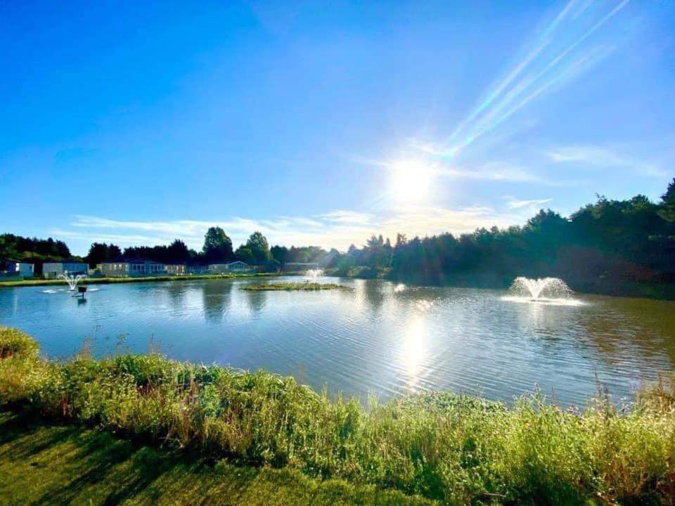 a lake with the sun shining on the water at Heathery Lodge with Hot Tub in York