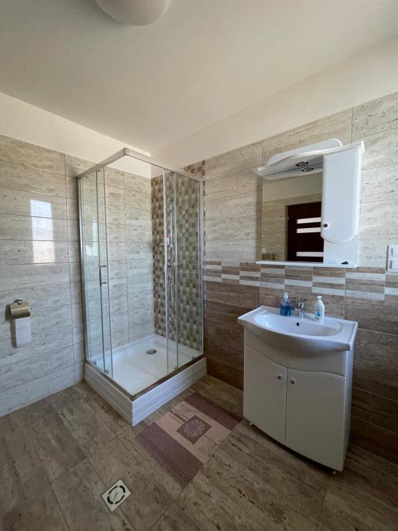 uma casa de banho com um chuveiro, um lavatório e um espelho. em Auróra Rendezvényterem & Szállás em Jászapáti