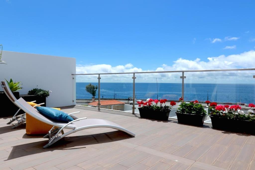 a deck with a chair and flowers and the ocean at Consuls Ocean View in Ponta Delgada