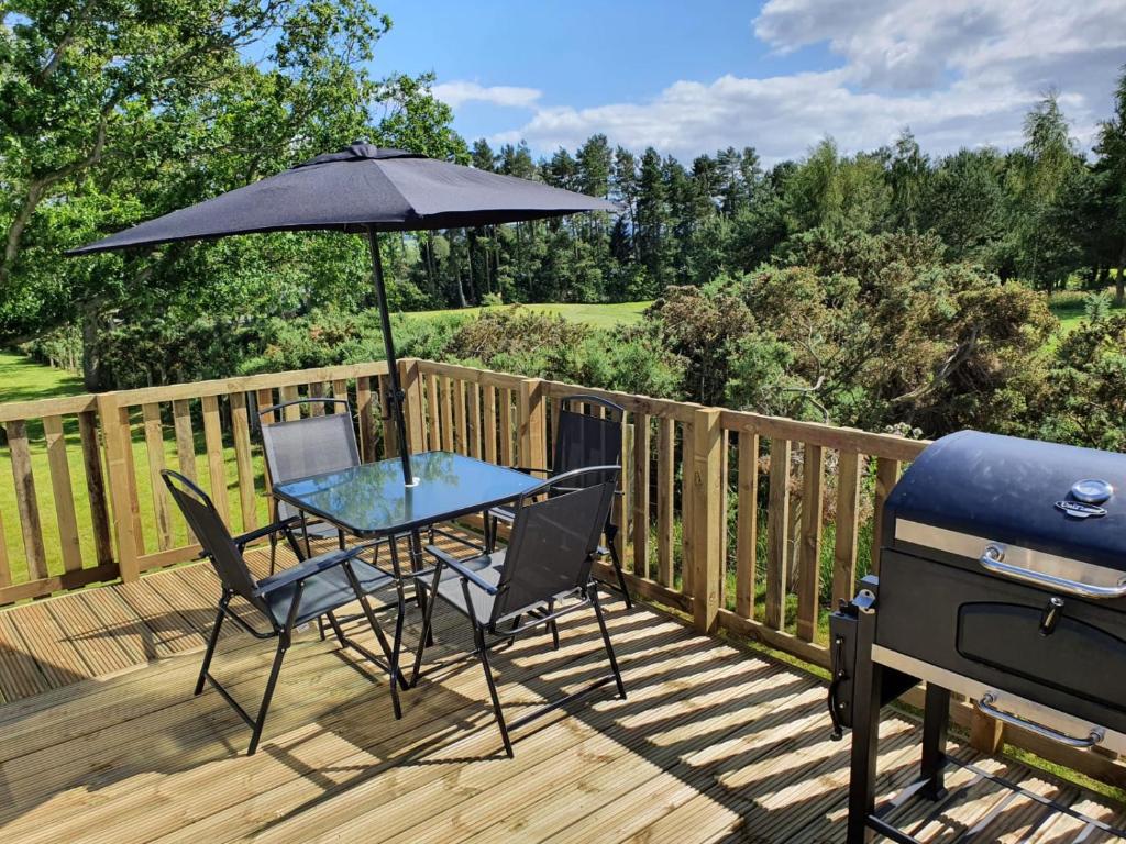 a grill and a table with an umbrella on a deck at Beautiful Borders Cabin in Jedburgh