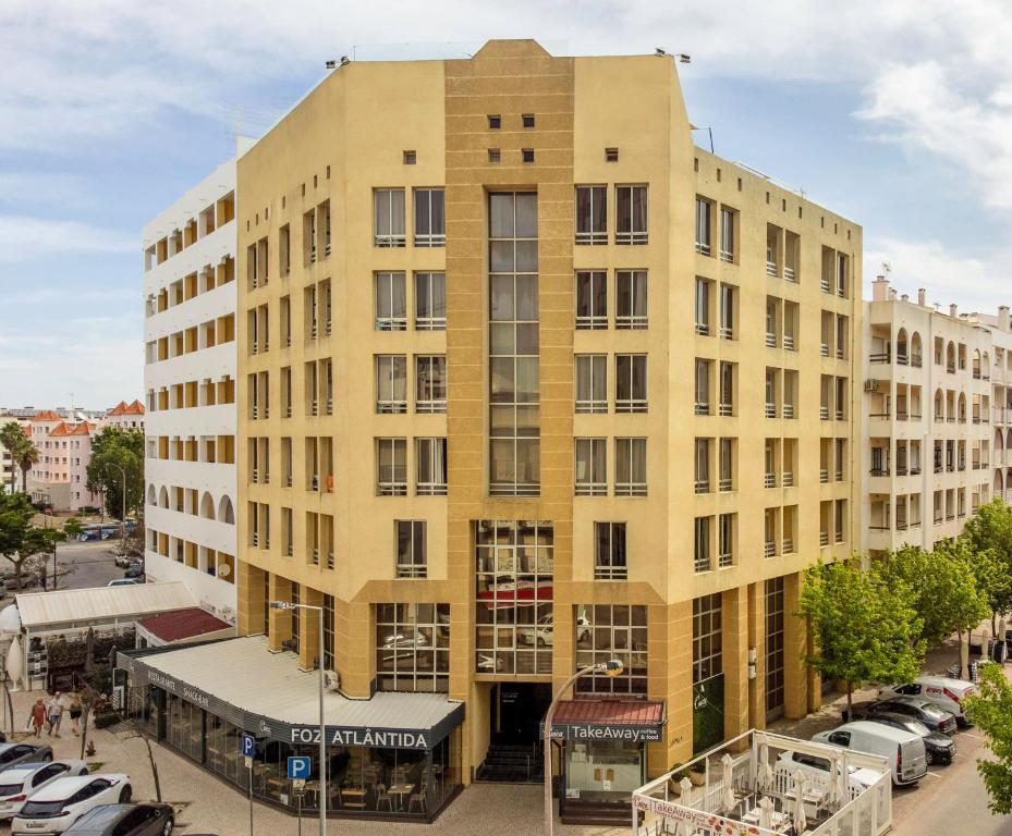 een groot geel gebouw met auto's geparkeerd op een parkeerplaats bij Hotel Apartamento Foz Atlantida in Monte Gordo