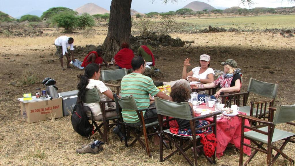 a group of people sitting at a table under a tree at Maasai Simba Camp in Amboseli