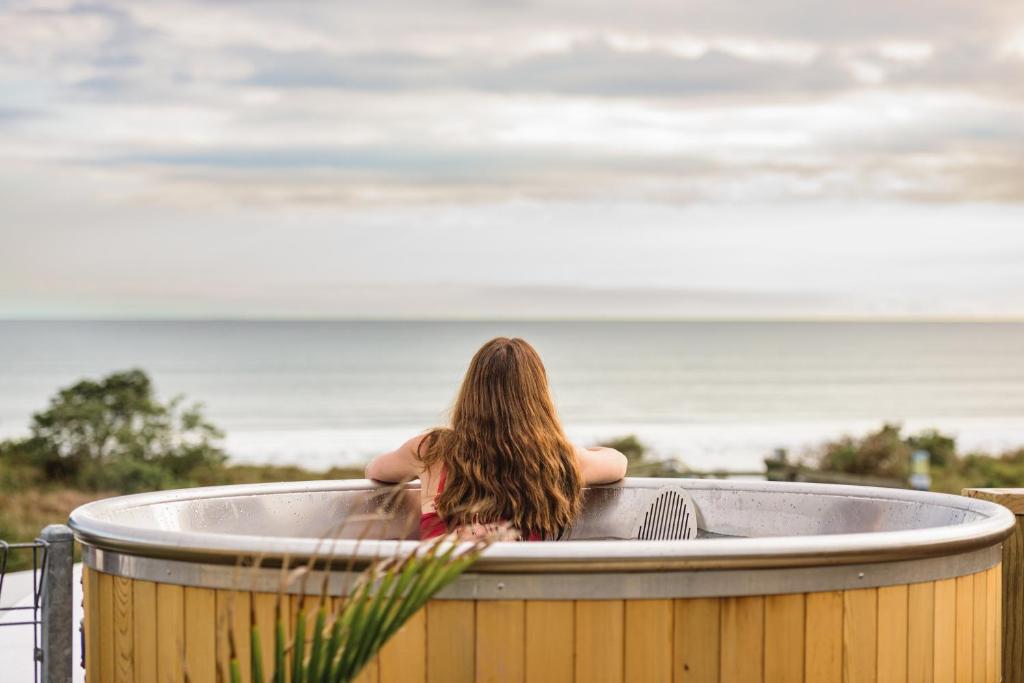 Una donna seduta in una vasca idromassaggio che guarda l'oceano di Ohope Beach TOP 10 Holiday Park a Ohope Beach