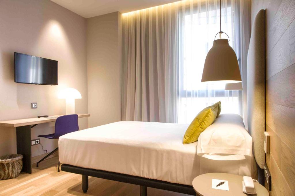 Una habitación de hotel con una cama, un escritorio y una ventana. en Zenit San Sebastián, en San Sebastián