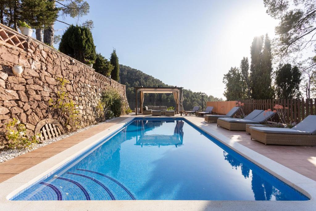 a swimming pool with chairs and a stone wall at Luxury Villa El Turo in Castellví de Rosanés