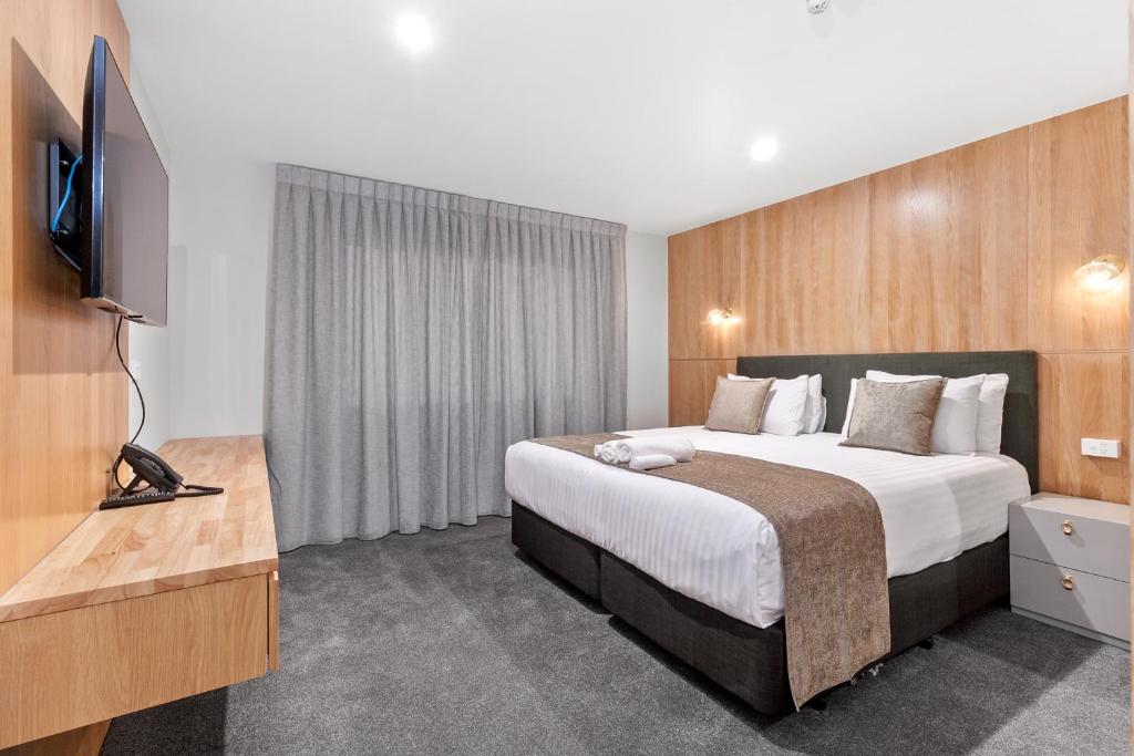 a hotel room with a bed and a flat screen tv at Kolmar Inn in Auckland