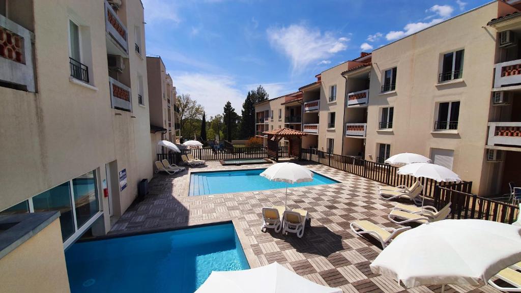 basen z leżakami i parasolami obok budynków w obiekcie Le Blanc-Martel - Piscine, Climatisation & Parking w mieście Gréoux-les-Bains