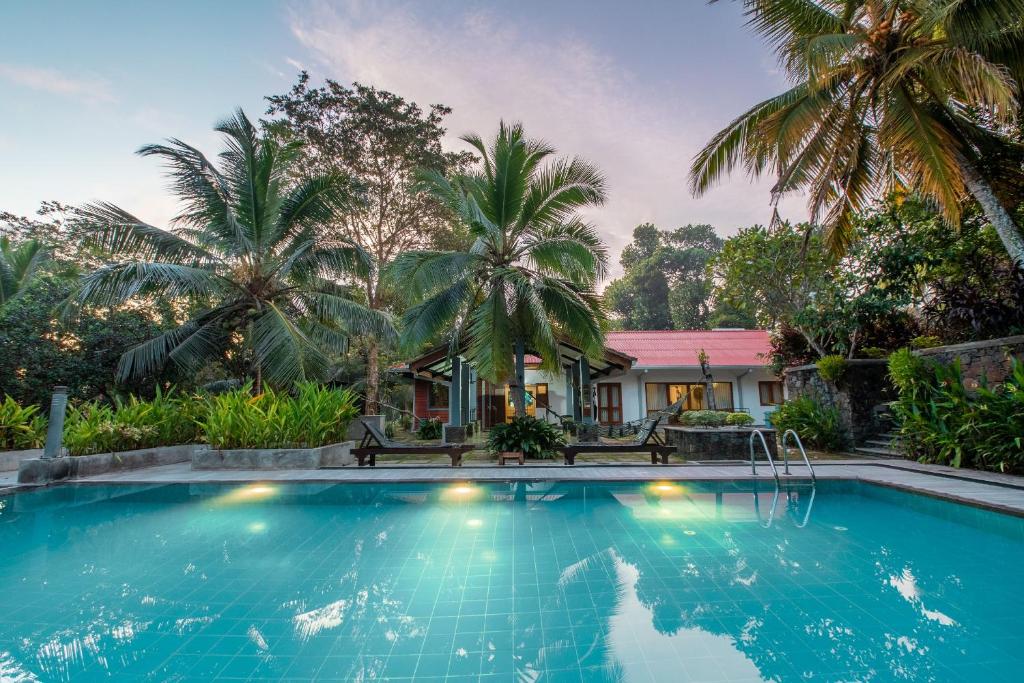 a swimming pool in front of a house with palm trees at Villa Acres Green in Hikkaduwa