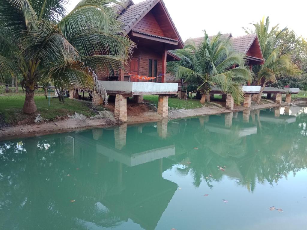 uma casa com palmeiras em frente a um corpo de água em Home Style Resort em Buri Ram