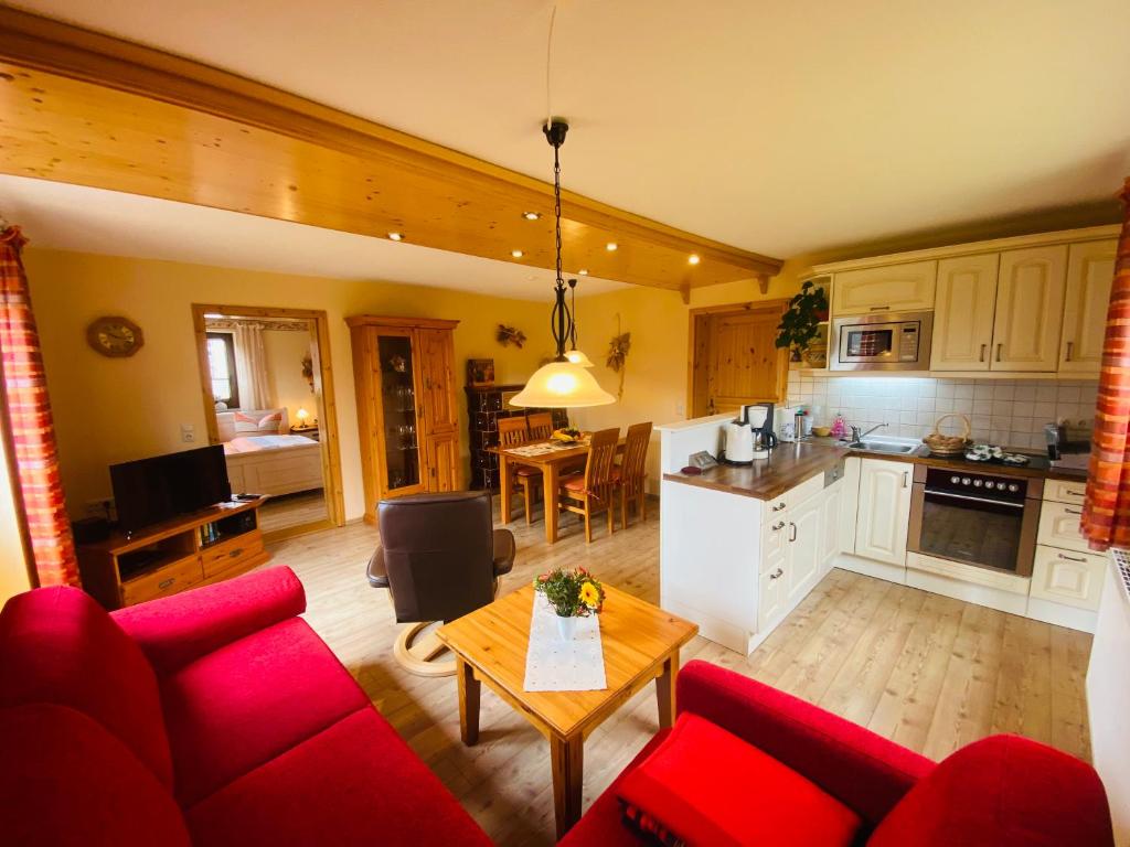 a living room with a red couch and a kitchen at Ferienhof Alte Wildmeisterei - Fewo Gartenblick in Neuhaus am Rennweg