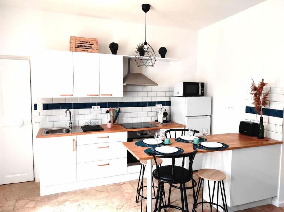 une cuisine avec des placards blancs et une table avec des tabourets dans l'établissement L'Antique SPA: jacuzzi sous patio, à Orange