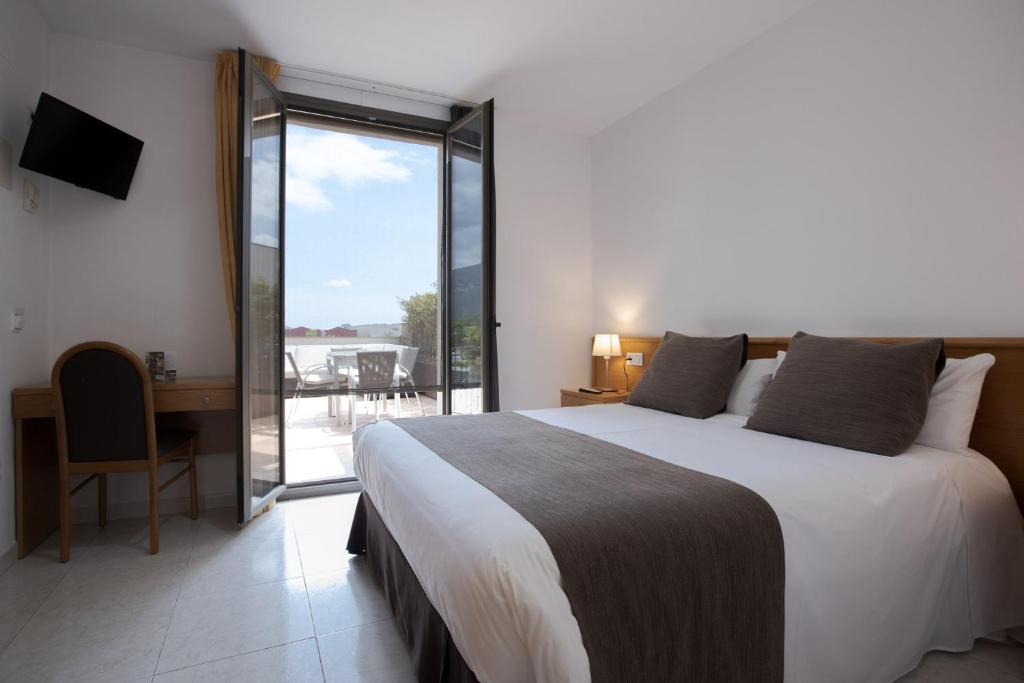 Schlafzimmer mit einem Bett, einem Schreibtisch und einem Balkon in der Unterkunft Hotel Alta Garrotxa in Tortellá