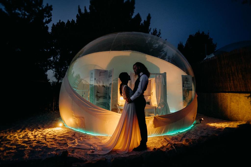Una novia y un novio parados dentro de un orbe redondo en Burbujas Astronómicas Albarari Sanxenxo, en Sanxenxo