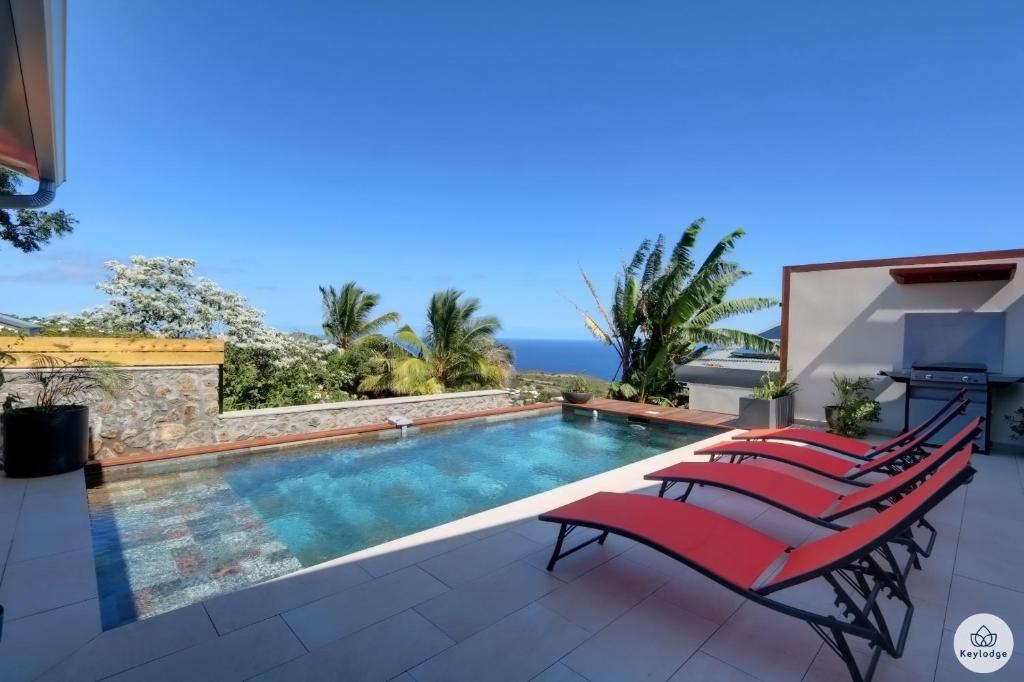 een zwembad met rode stoelen en de oceaan op de achtergrond bij Villa Aïna - Piscine 4 étoiles - Vue mer - Saint Leu in Saint-Leu