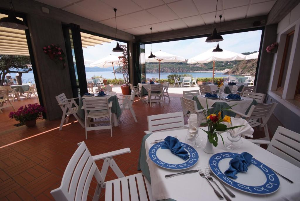 a restaurant with white tables and chairs with a view of the ocean at Hotel Dino in Capoliveri