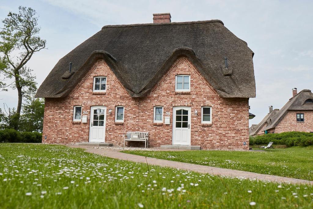 una casa con techo de paja en un campo de césped en Beach House Reetdachhaus Beach House 2 en Tating