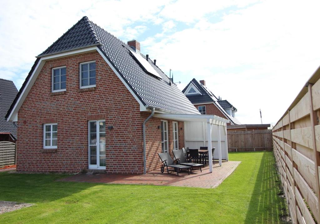 a brick house with a patio and a fence at Ferienhaus Westwind Einzelhaus Westwind in Brösum