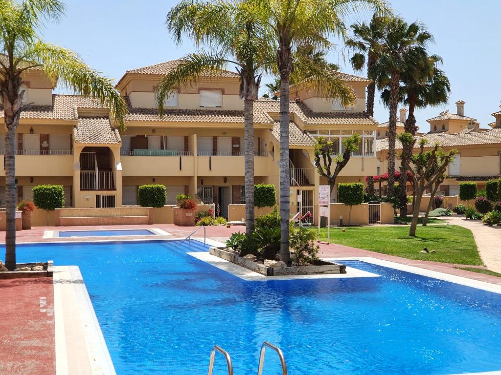 una piscina di fronte a un edificio con palme di The Hideaway 2 Bed Poolside Groundfloor Apartment On Albatros Full AC Free Fast Wifi a Los Alcázares