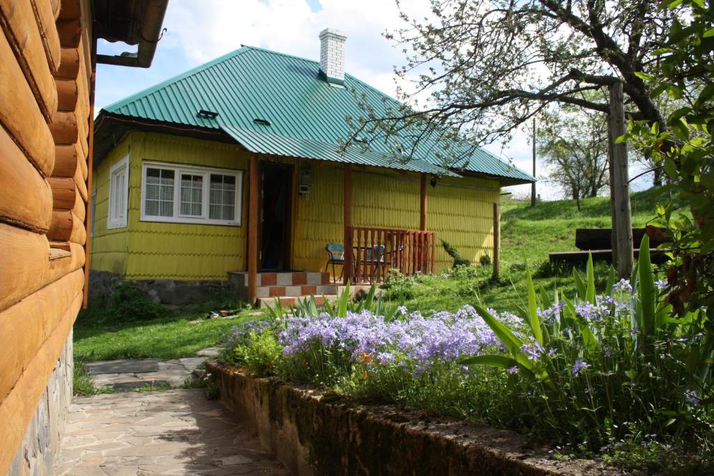 a yellow house with purple flowers in front of it at Sadyba Lukacha in Zhdenievo