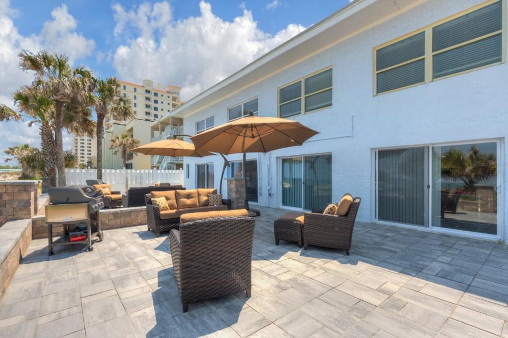 a patio with chairs and an umbrella in front of a building at Shore To Please Beach Oceanfront Patio Pet Friendly in Jacksonville Beach