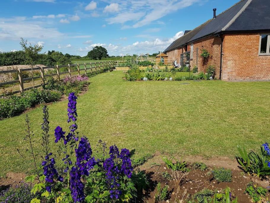 - un jardin avec des fleurs violettes à côté d'un bâtiment en briques dans l'établissement Sweet Meadow Lodge, à Exeter