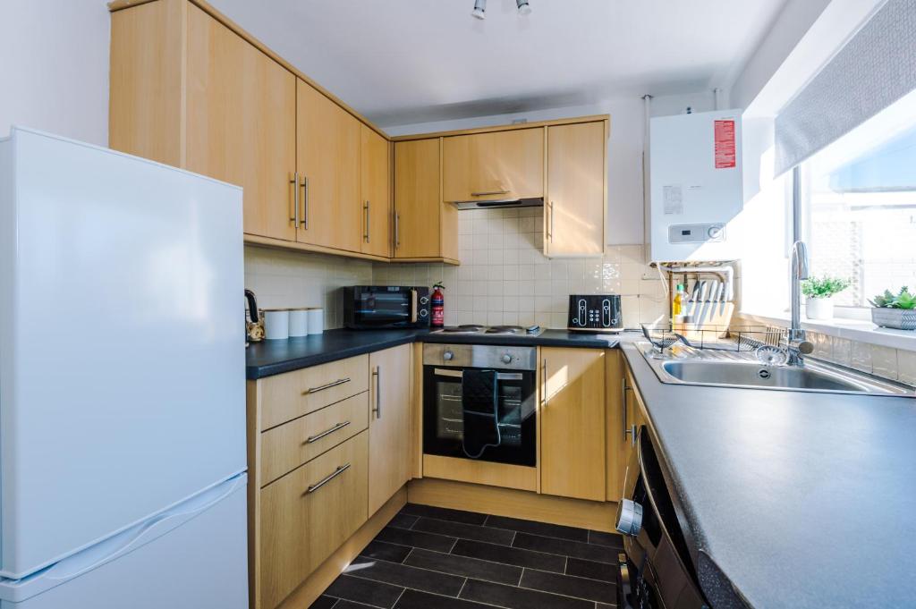 a kitchen with wooden cabinets and a sink and a refrigerator at Cheerful 3 bedroom home with parking in Chester in Saughall