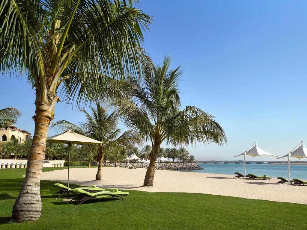 a beach with palm trees and chairs and the ocean at Traders Hotel, Abu Dhabi in Abu Dhabi