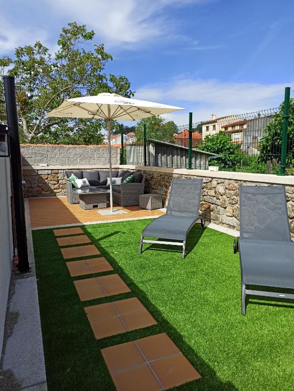 a patio with two chairs and an umbrella and grass at A casiña de Estela in Caldas de Reis