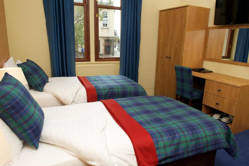 a hotel room with two beds and a desk and window at The Pipers' Tryst Hotel in Glasgow