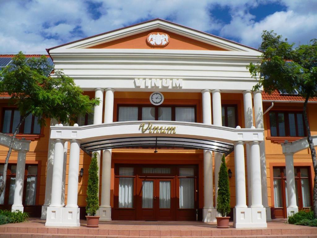 ein orangefarbenes und weißes Gebäude mit einer Uhr drauf in der Unterkunft Vinum Hotel in Kiskőrös