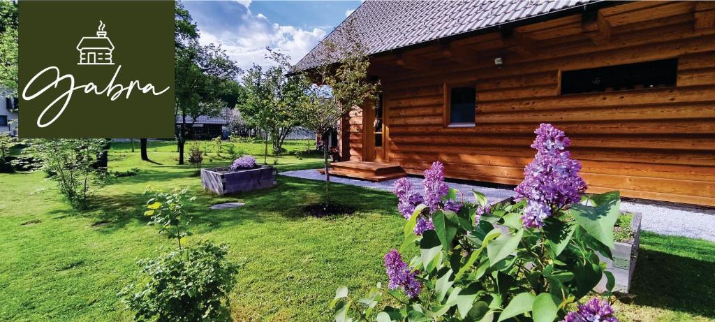 una cabaña de madera con flores púrpuras delante de ella en Wooden House Gabra en Podnart