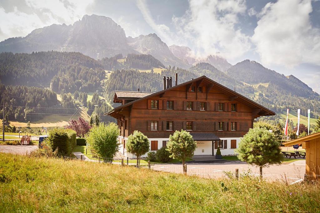a large wooden building with mountains in the background at Reka-Ferienanlage Rougemont in Rougemont