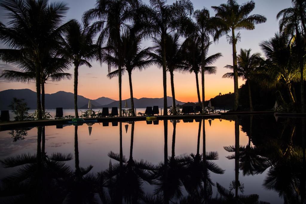 una piscina con palmeras frente a la puesta de sol en Corsário Hotel, en Ubatuba