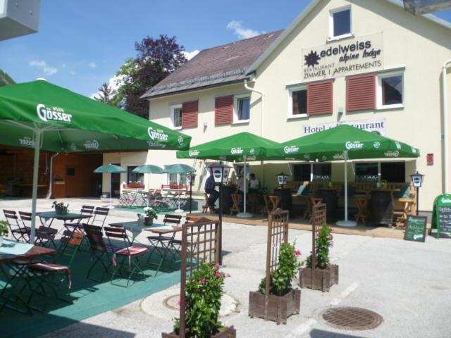 ein Restaurant mit Tischen, Stühlen und grünen Sonnenschirmen in der Unterkunft Hotel & Restaurant Edelweiss Alpine Lodge in Hinterstoder