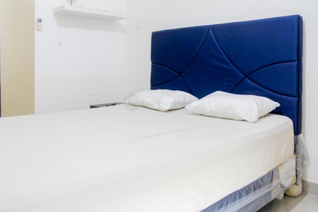 RedLiving Apartemen Paradise Mansion - Gunawan في جاكرتا: سرير مع اللوح الأمامي الأزرق ووسادتين بيضاء