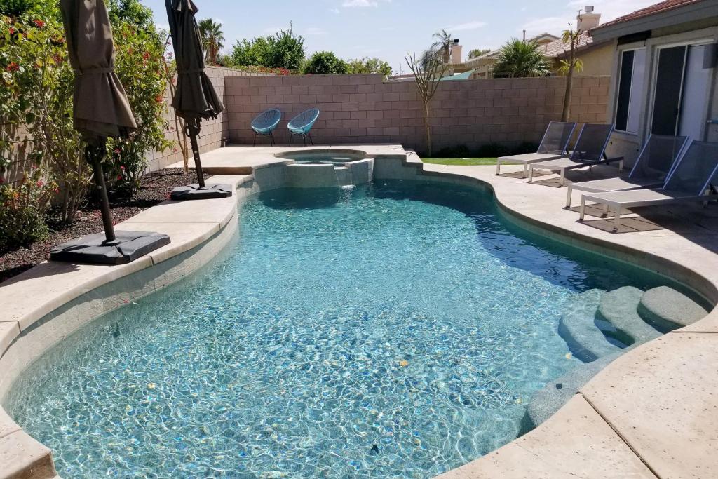 a swimming pool in a backyard with chairs and an umbrella at Deerbrook Manor Permit# 67085 in La Quinta