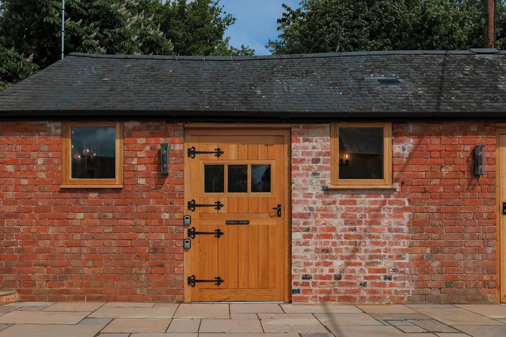 a brick garage with a wooden door and windows at Eakley Stables 3 - Weiser in Stoke Goldington