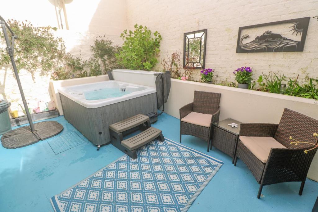 a hot tub sitting on a patio with chairs at Driftwood in Marazion