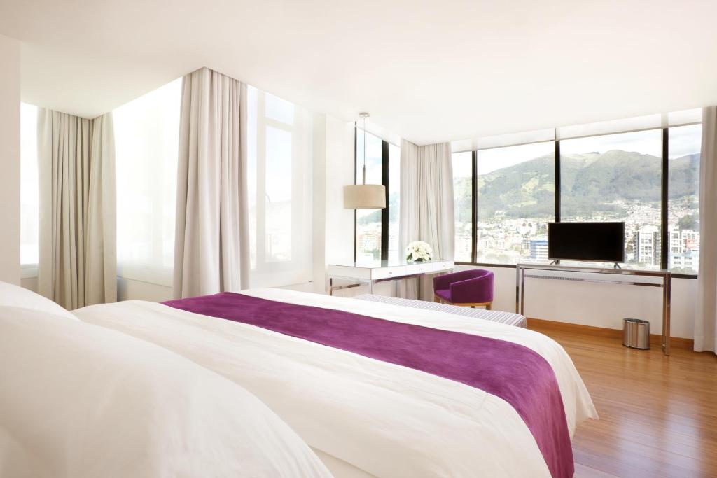 a white bedroom with a large bed and a television at Hotel Rio Amazonas in Quito