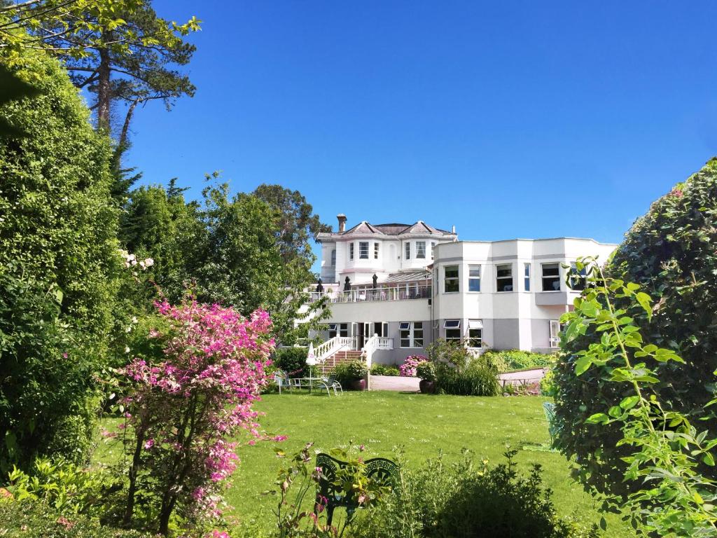 ein großes weißes Haus mit einem Hof mit rosa Blumen in der Unterkunft Abbey Sands Hotel in Torquay