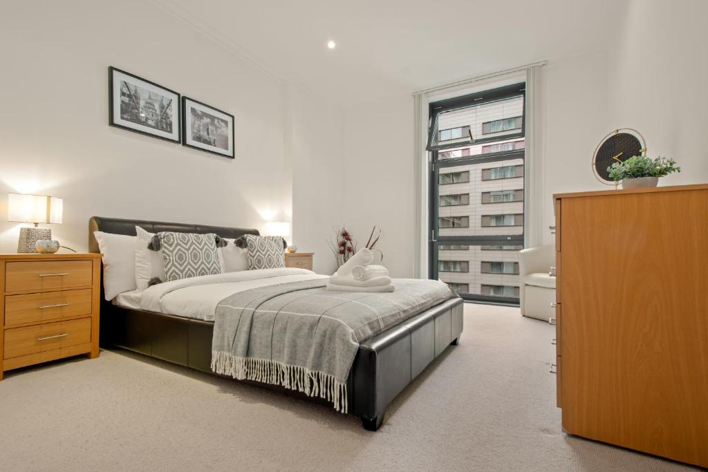 a bedroom with a bed and a dresser and a window at South Quay Apartments Canary Wharf in London