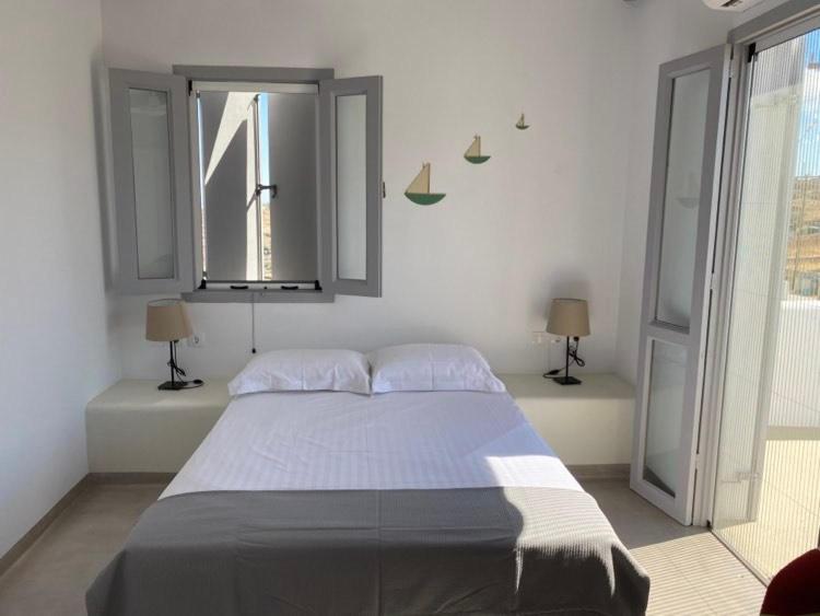 a bedroom with a large bed with two windows at Maganiotis Rooms in Kimolos