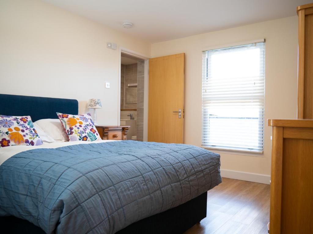 a bedroom with a bed with a blue blanket and a window at Ellingham Apartments, Bordeaux Harbour, Guernsey in Vale