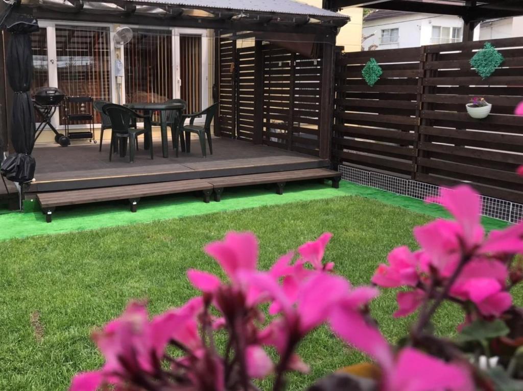 un patio con mesa, sillas y flores rosas en Guest House モモ en Obihiro