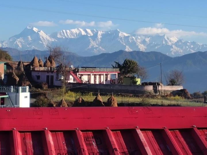 a red building with mountains in the background at Odyssey Stays Majkhali, Ranikhet in Chaubattia