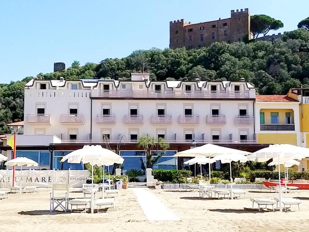 un edificio con sedie e ombrelloni su una spiaggia di Hotel Miramare a Castiglione della Pescaia