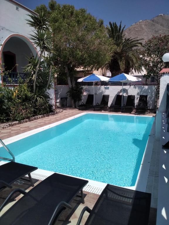 a blue swimming pool with chairs and umbrellas at Studios Irineos in Perissa