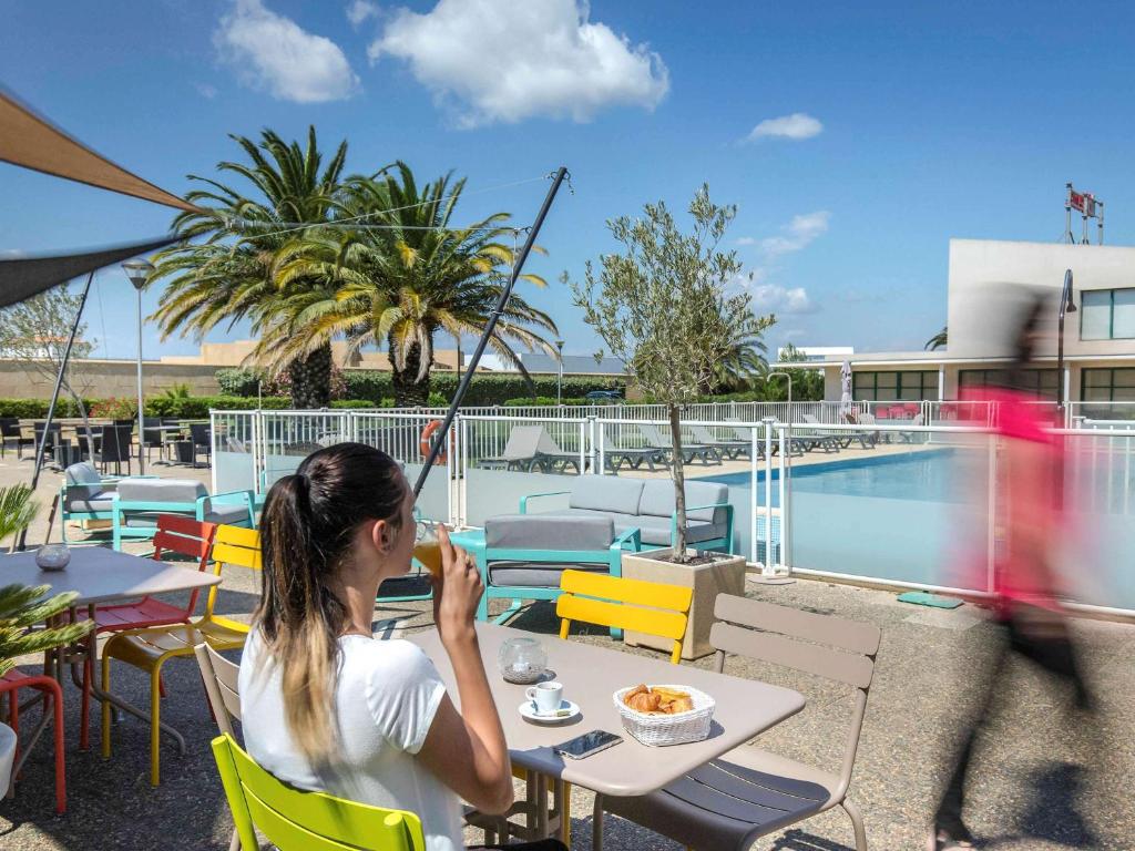 une femme assise à une table avec un verre dans l'établissement Novotel Perpignan Nord Rivesaltes, à Rivesaltes