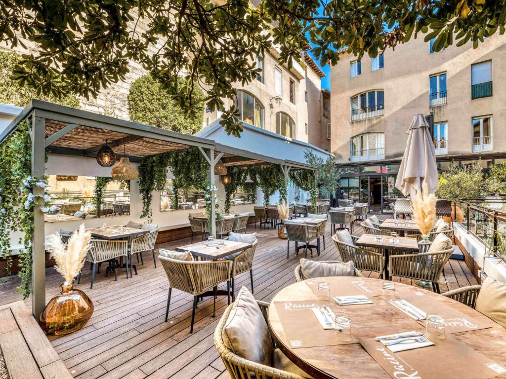 una terraza de madera con mesas, sillas y edificios en Mercure Pont d’Avignon Centre en Aviñón